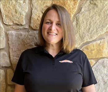 Woman wearing a black servpro polo is standing in front of a rock wall smiling