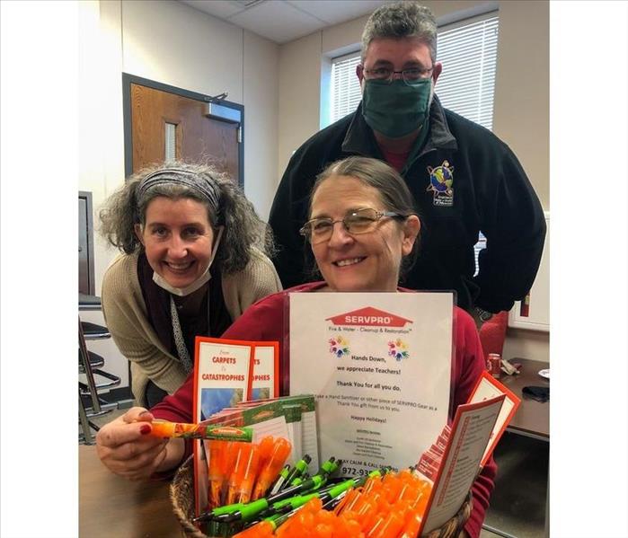 Two female and one male teacher displaying basket of small hand sanitizers and pens from SERVPRO